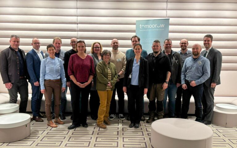 Gruppenfoto von 17 Personen bei der Gründung der Arbeitsgruppe „Biomasse“ im Rahmen des Projekts„tomoorow. Die Personen stehen in zwei Reihen vor einem Roll-Up mit Projektlogo.