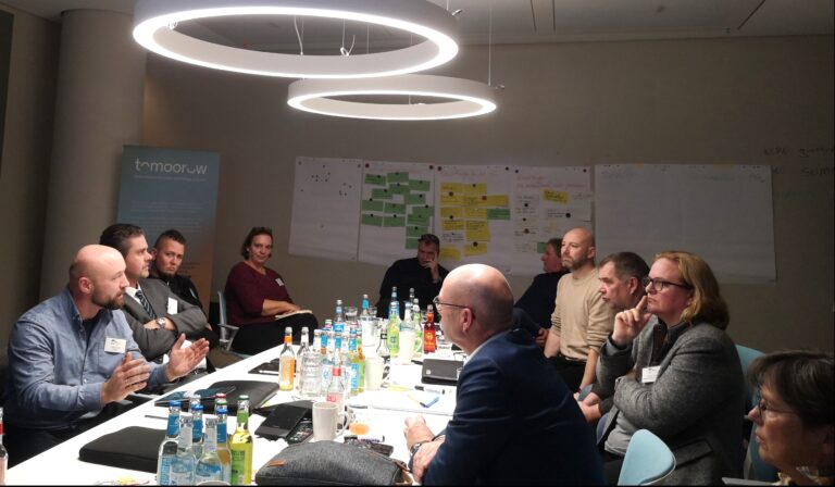 Mitglieder der AG Landwirtschaft der PaludiAllianz bei einer intensiven Diskussionsrunde. Die Gruppe sitzt an einem Tisch, umgeben von Flipcharts und Materialien, und tauscht sich über Paludikultur und Wertschöpfung aus.